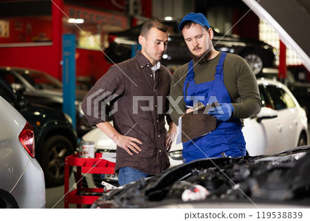 Male worker of auto service speaking to man client concerning his notes on paper Male worker of auto service speaking to man client concerning his notes on paper 119538839