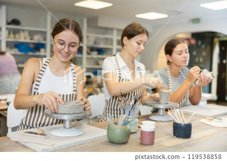 Three craftsperson are busy sculpting from clay and painting ceramic products 119538858