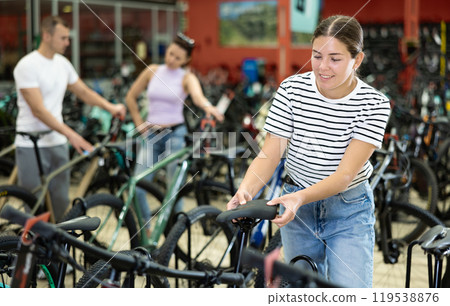 Smiling young girl choosing model seat on high-speed bike in sports shop Smiling young girl choosing model seat on high-speed bike in sports shop 119538876