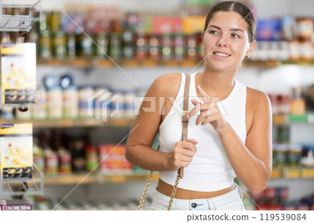 Girl in supermarket sales area looks into distance and searches for necessary goods Girl in supermarket sales area looks into distance and searches for necessary goods 119539084