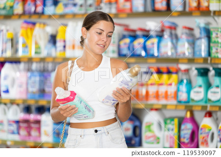 Woman carefully selects cleaning product in industrial section of supermarket 119539097