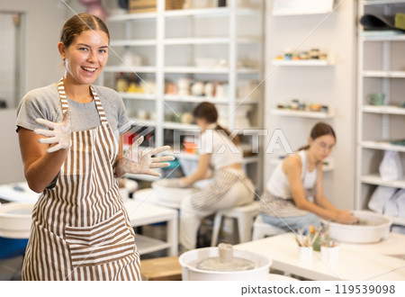 Girl takes break, stands and rests, waves hello with her hands stained with clay during pottery class 119539098