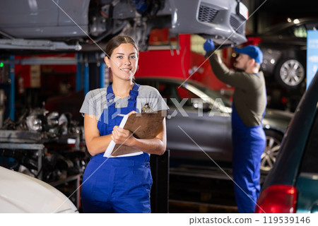 Female car service worker keeps records of work performed by auto mechanics in car service station - makes notes on paper 119539146