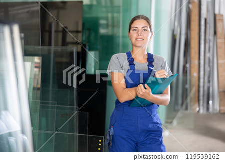 Female worker checks the quality of made window glass in an industrial workshop, marks the data in documents Female worker checks the quality of made window glass in an industrial workshop, marks the data in documents 119539162