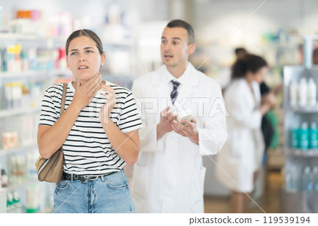Young girl feeling pain standing with her back to male pharmacist offering remedy 119539194