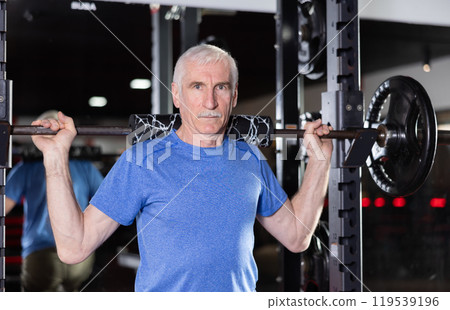 Elderly man training with barbell in gym 119539196