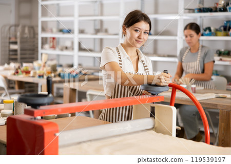 Girl student in pottery workshop works with machine clay press roller 119539197