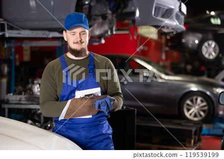 Mechanic guy posing with documents in car service station 119539199