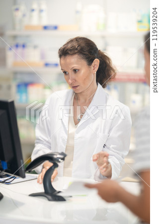 Middle-aged female pharmacist speaking to woman customer buying medicinal preparation in drugstore 119539204