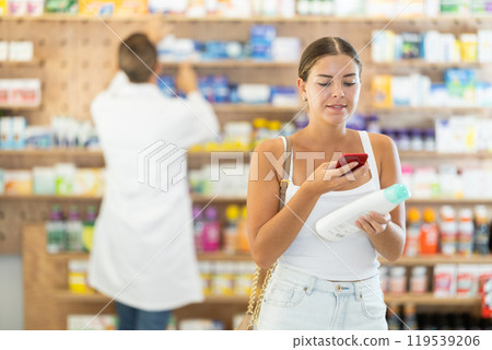 In pharmacy girl customer scans code on shampoo label, photographs packaging. 119539206