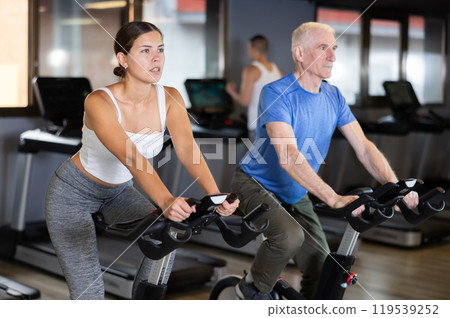 Concentrated young girl working out on stationary bicycle in gym. Healthy active lifestyle concept Concentrated young girl working out on stationary bicycle in gym. Healthy active lifestyle concept 119539252