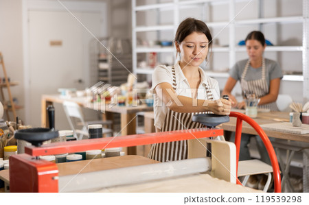 Girl student in pottery workshop works with machine clay press roller Girl student in pottery workshop works with machine clay press roller 119539298