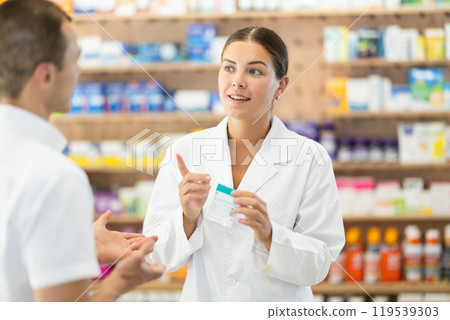 Female pharmacist consulting young guy about medicament in box Female pharmacist consulting young guy about medicament in box 119539303