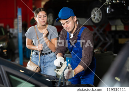 Young guy mechanic fixing woman client's car Young guy mechanic fixing woman client's car 119539311