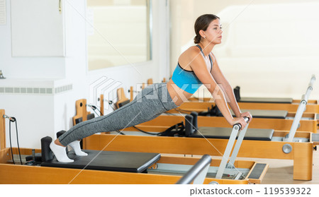 Girl doing stretching exercises on reformer in pilates studio Girl doing stretching exercises on reformer in pilates studio 119539322