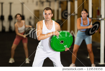 Closeup of athletic sports man standing with plate of barbell in hands in fitness studio Closeup of athletic sports man standing with plate of barbell in hands in fitness studio 119539350