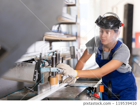 Workwoman cutting PVC profile on industrial machine in workshop Workwoman cutting PVC profile on industrial machine in workshop 119539410