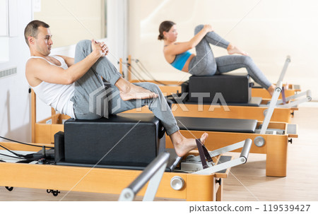 Sporty man in sports wear engages in Pilates on reformer machine 119539427