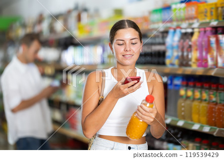 Girl scans qr code on soda or juice label in supermarket 119539429