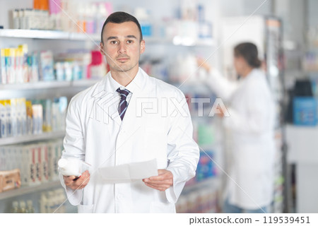 Young male pharmacist holding plastic bottle of medicine and recipe 119539451
