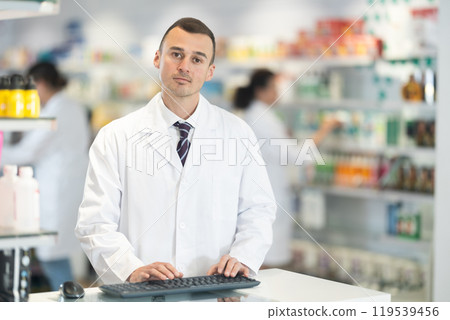 Young male pharmacist posing at computer in pharmacy 119539456