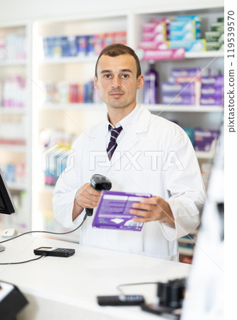 Man pharmacist in cash area works with computer and goods, scans drugs, checks availability Man pharmacist in cash area works with computer and goods, scans drugs, checks availability 119539570