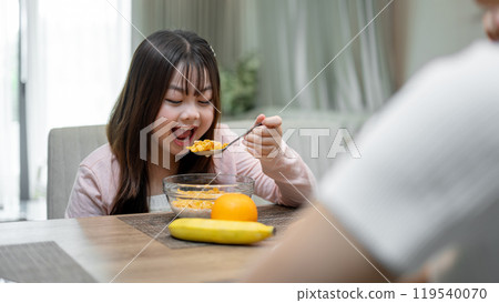 A young, happy Asian girl is enjoying a conversation with her mom while having breakfast. 119540070