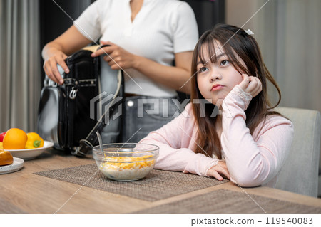 A young, stubborn Asian girl at the dining table, refusing to have breakfast before going to school. 119540083