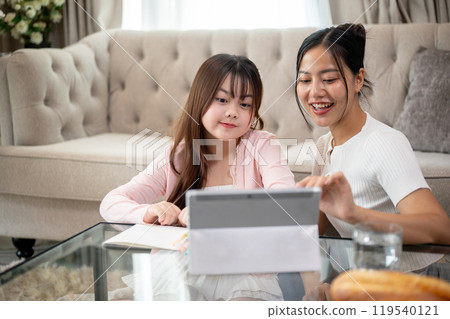A young cute Asian girl and her mother are enjoying watching a cartoon on a tablet together at home. 119540121