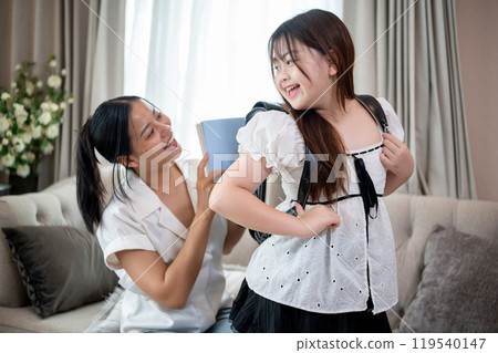 Caring Asian mom is helping her young daughter prepare for school, enjoying a conversation together. 119540147