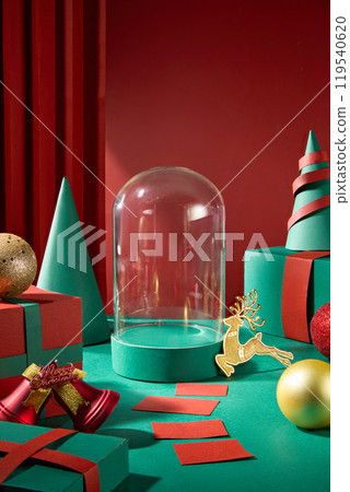 The image shows a Christmas-themed display featuring a clear glass dome on a green podium. Gift boxes and Noel decorations surround the display against a bright red backdrop. 119540620