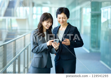 Two businesswomen in suits looking at their smartphones 119541293