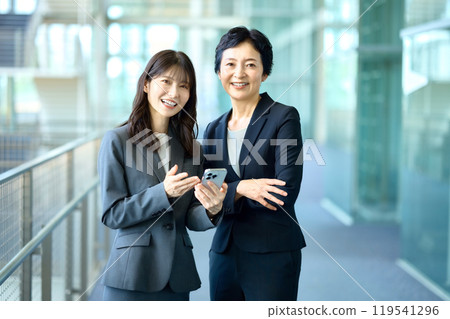 Two businesswomen in suits looking at their smartphones 119541296