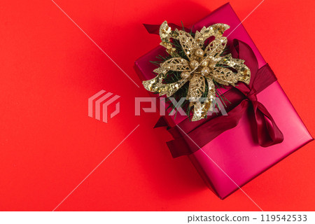 Gift box with ribbon bow golden flower decoration on red background 119542533