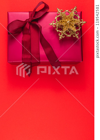 Festive gift box with bow and golden decorative star on red background 119542581
