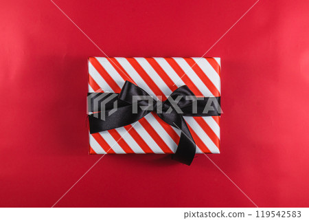 Red gift box with white stripes and a black bow on a red background 119542583