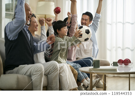 three generation asian family watching soccer game telecast on tv together at home three generation asian family watching soccer game telecast on tv together at home 119544353
