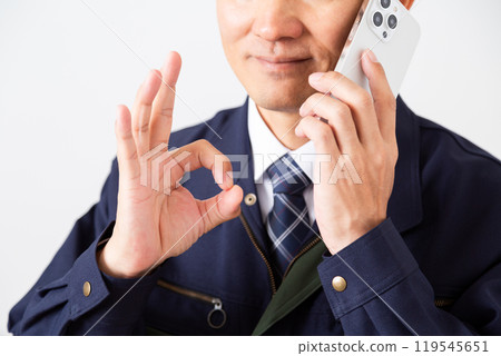 A middle-aged male businessman in work clothes making a circle sign while talking on a smartphone 119545651