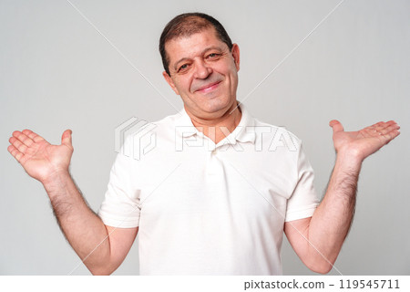 Smiling man in a white shirt gestures with open palms against a light gray background Smiling man in a white shirt gestures with open palms against a light gray background 119545711