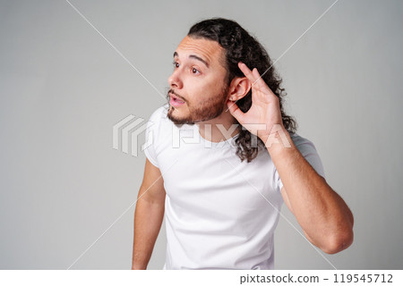 A young man with curly hair listening attentively while standing against a plain background A young man with curly hair listening attentively while standing against a plain background 119545712