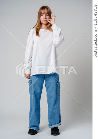 A young woman holding her finger to her lips, signaling silence in a minimalist studio 119545718