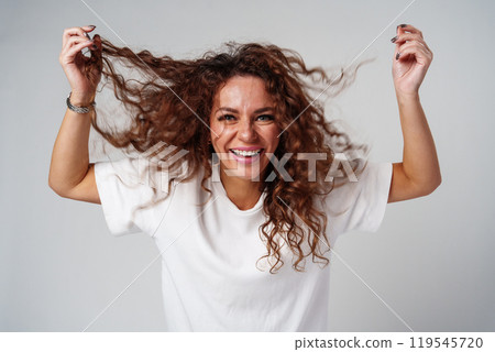 A woman in a white shirt and ripped jeans posing positively with a playful expression in a light studio setting 119545720