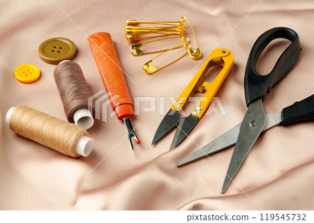 Sewing tools and materials arranged on a luxurious golden fabric background in a creative crafting workspace 119545732