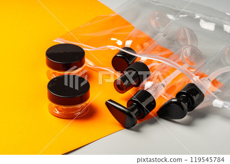 Travel-sized containers arranged neatly in a clear bag on a contrasting orange and gray background 119545784