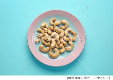 A close-up view of raw cashews arranged on a pastel pink plate against a vibrant turquoise 119546921