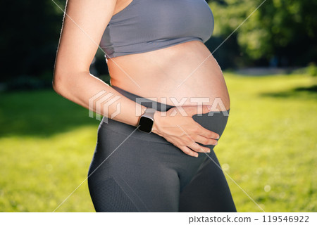 Unrecognizable pregnant woman in sportswear holding her belly outdoors 119546922