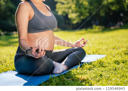 Pregnant woman exercising in park enjoying warm summer sun practicing yoga on green grass 119546943