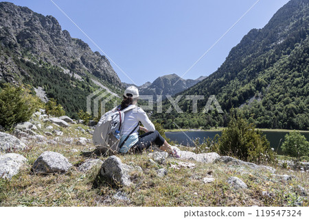 Female backpacker tourist in Spain looking at landscape while sitting on the rock in front of a lake. 119547324
