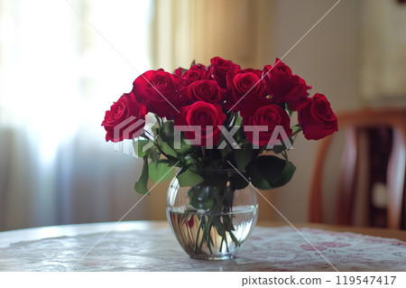 A vibrant bouquet of red roses in a glass vase on a table in a warmly lit room, capturing a moment 119547417
