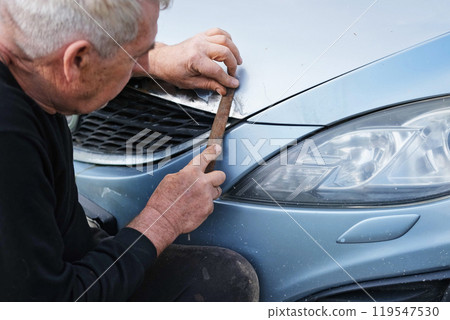 Car body shop. Repair man processes the welding seam using an angle grinder on replaced car part. Professional Body master grind old paint and rust. Rusty damage. Rusting car. Hands with tool close-up 119547530